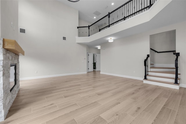 unfurnished living room with a stone fireplace, light wood-type flooring, and a towering ceiling