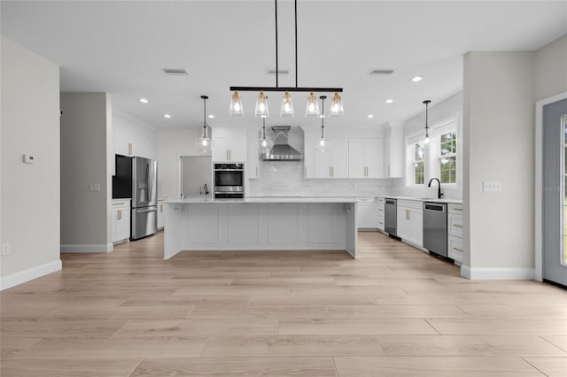 kitchen featuring stainless steel appliances, wall chimney range hood, hanging light fixtures, decorative backsplash, and a center island