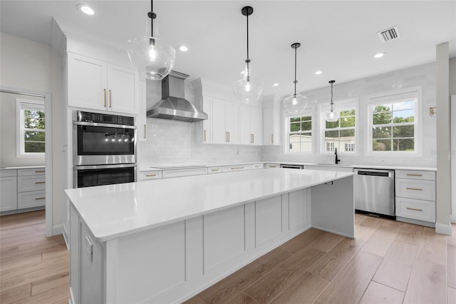 kitchen featuring stainless steel appliances, wall chimney range hood, backsplash, light wood-type flooring, and a center island