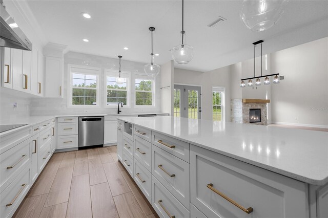 kitchen featuring pendant lighting, light wood-type flooring, wall chimney exhaust hood, dishwasher, and a stone fireplace