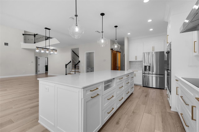 kitchen featuring backsplash, stainless steel appliances, light hardwood / wood-style floors, hanging light fixtures, and a spacious island