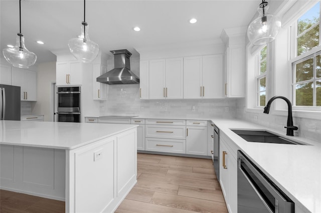 kitchen with appliances with stainless steel finishes, decorative backsplash, light wood-type flooring, and wall chimney exhaust hood