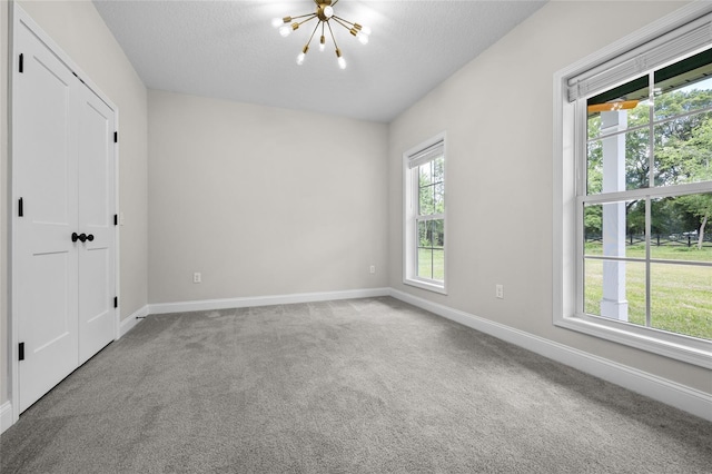 empty room featuring light carpet, a wealth of natural light, and a chandelier