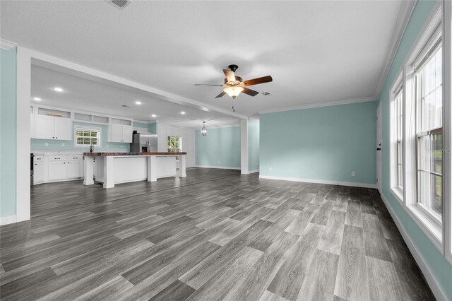 unfurnished living room with wood-type flooring, ornamental molding, a wealth of natural light, and ceiling fan