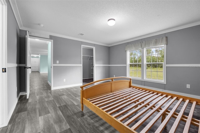 unfurnished bedroom featuring a spacious closet, a closet, crown molding, a textured ceiling, and dark wood-type flooring