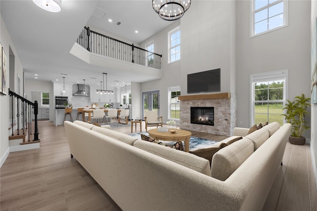 living room with a fireplace, light hardwood / wood-style floors, a notable chandelier, and a high ceiling