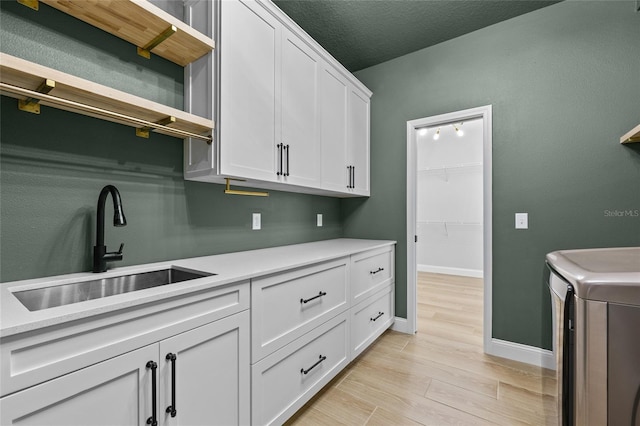 washroom with washing machine and dryer, sink, cabinets, light wood-type flooring, and a textured ceiling