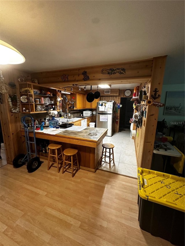 kitchen with a kitchen breakfast bar, light wood-type flooring, stainless steel refrigerator, and kitchen peninsula