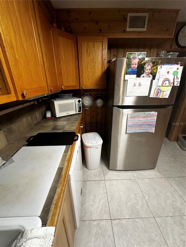 4215 NW 10th St, Gainesville, FL 32609 - kitchen with white microwave, freestanding refrigerator, tile counters, brown cabinets, and light tile patterned floors