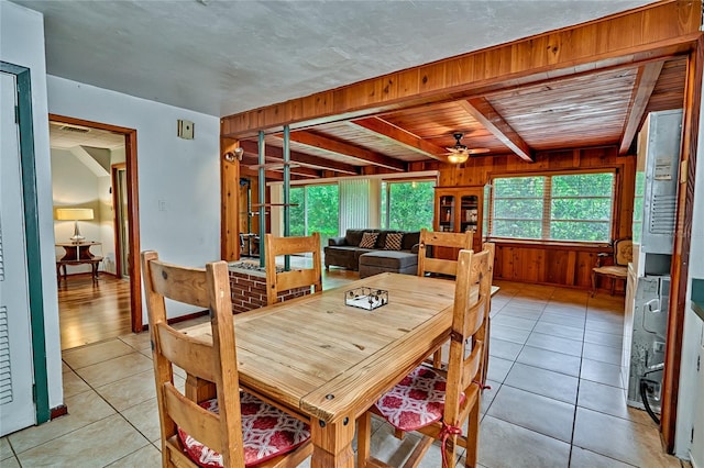 tiled dining space featuring ceiling fan, wood ceiling, beamed ceiling, and wooden walls