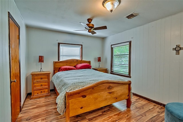 bedroom with ceiling fan, light hardwood / wood-style flooring, wooden walls, and multiple windows