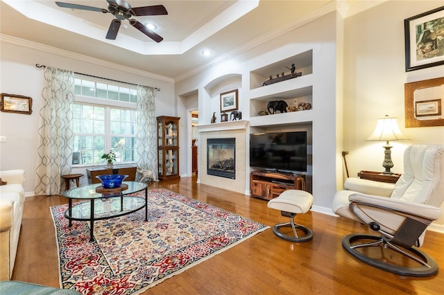 living room featuring a tile fireplace, wood-type flooring, ceiling fan, and a raised ceiling