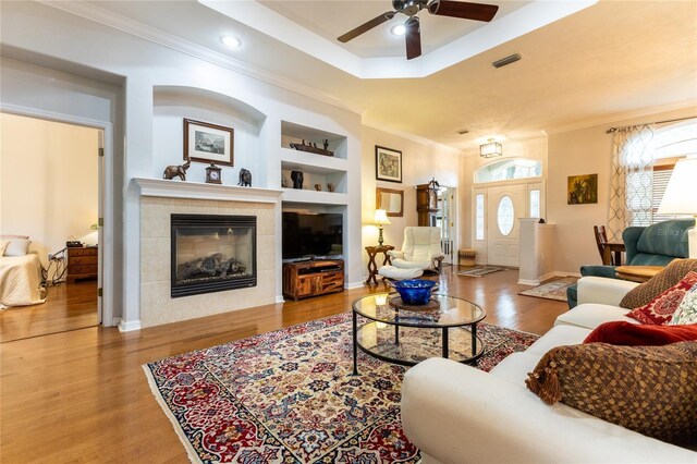 living room with built in shelves, a tile fireplace, hardwood / wood-style floors, and ceiling fan