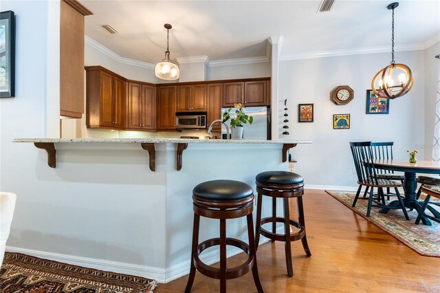 kitchen featuring stainless steel appliances, light hardwood / wood-style floors, crown molding, and a kitchen bar