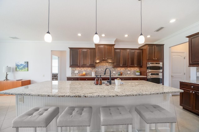 kitchen with hanging light fixtures, stainless steel double oven, and a kitchen island with sink