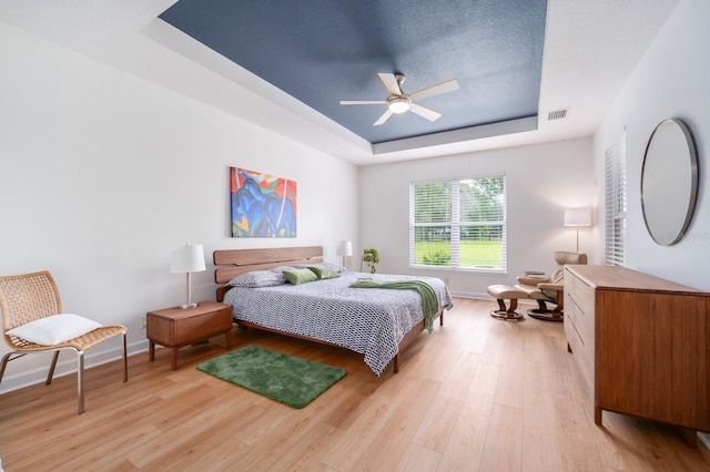 bedroom featuring ceiling fan, light hardwood / wood-style floors, and a tray ceiling