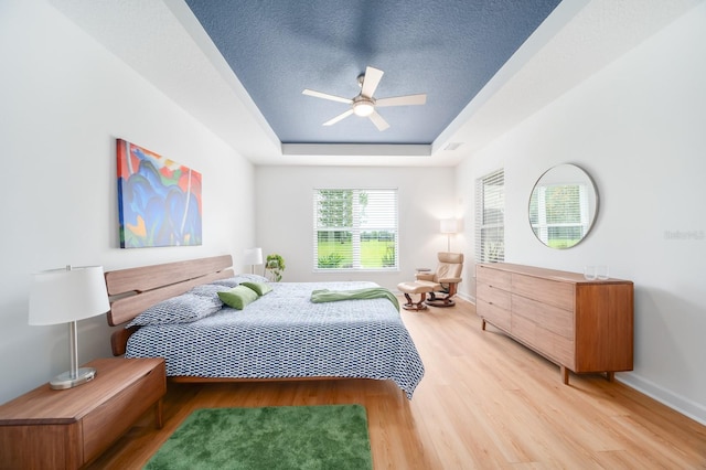 bedroom with a textured ceiling, ceiling fan, wood-type flooring, and a tray ceiling