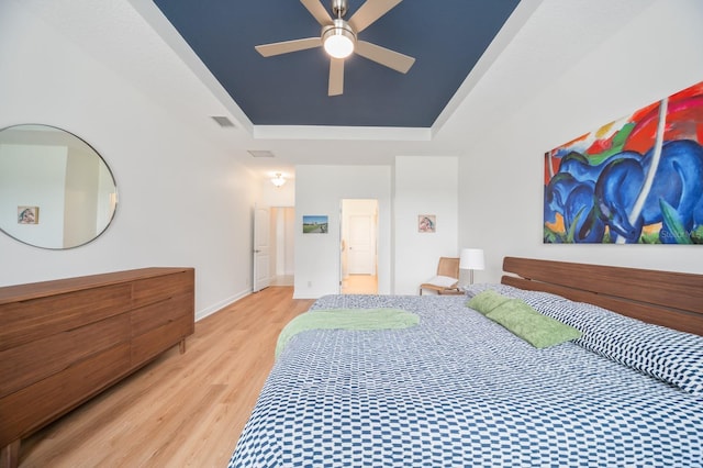 bedroom with light wood-type flooring, ceiling fan, and a tray ceiling