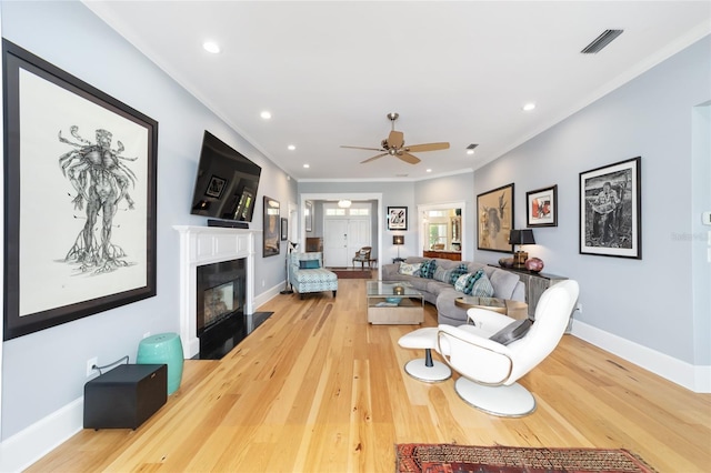 living room with light wood finished floors, a fireplace with flush hearth, visible vents, and ornamental molding