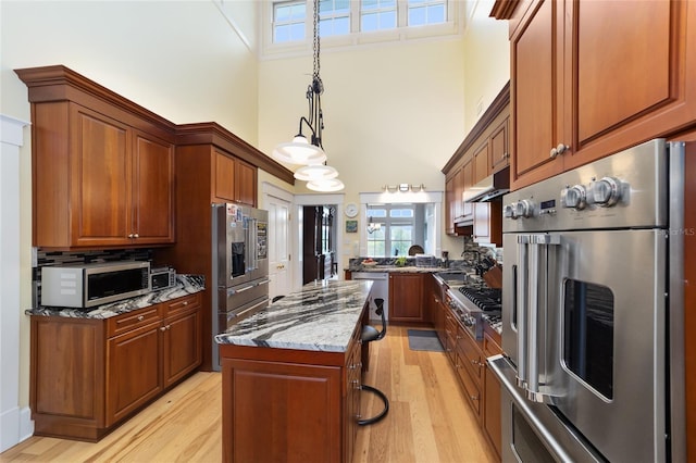 kitchen featuring stainless steel appliances, a center island, light stone counters, light hardwood / wood-style floors, and decorative light fixtures