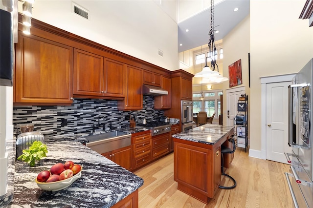 kitchen with stainless steel appliances, a center island, pendant lighting, dark stone counters, and a high ceiling