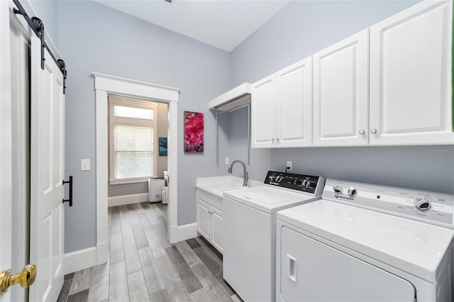 laundry room featuring sink, cabinets, independent washer and dryer, a barn door, and light wood-type flooring