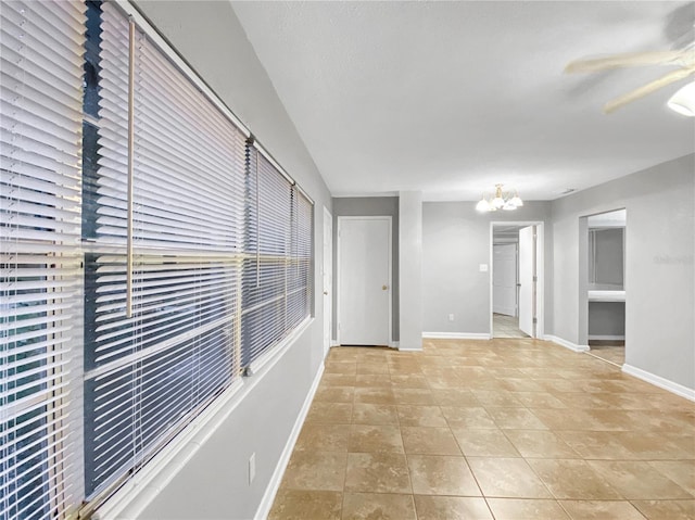 tiled empty room with ceiling fan with notable chandelier