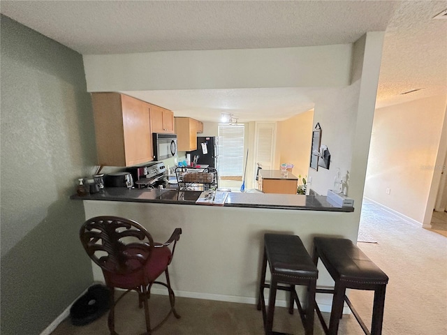 kitchen featuring a kitchen bar, black appliances, kitchen peninsula, light colored carpet, and a textured ceiling