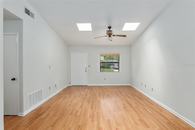 unfurnished room featuring light wood-type flooring, a skylight, visible vents, and baseboards