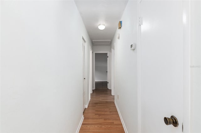 hallway featuring wood finished floors, attic access, and baseboards