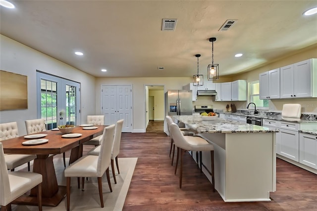 kitchen featuring white cabinetry, a center island, dark wood-type flooring, stainless steel appliances, and decorative light fixtures