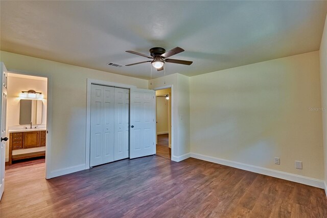 unfurnished bedroom featuring ensuite bath, ceiling fan, wood-type flooring, a closet, and sink