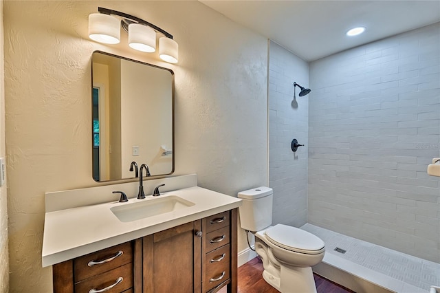 bathroom with vanity, hardwood / wood-style flooring, toilet, and tiled shower