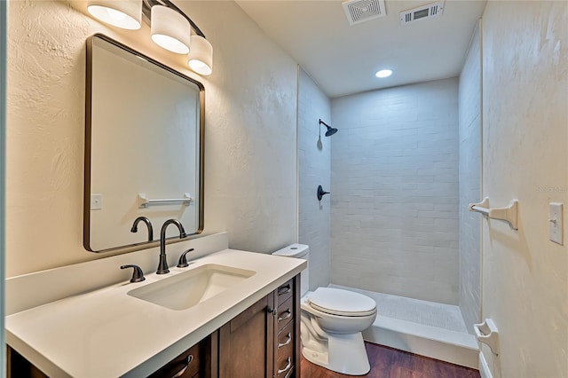 bathroom with toilet, hardwood / wood-style floors, vanity, and a tile shower