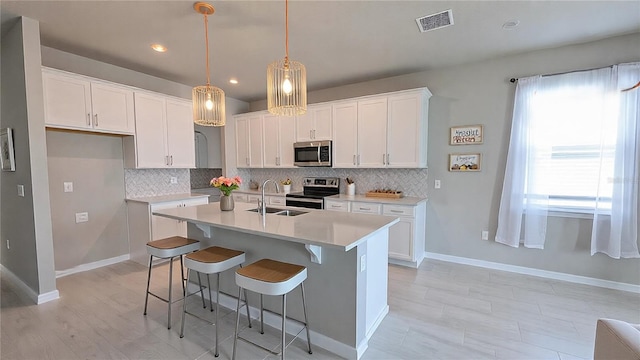 kitchen featuring sink, white cabinetry, appliances with stainless steel finishes, an island with sink, and pendant lighting