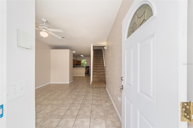 foyer entrance with baseboards, stairway, a ceiling fan, and light tile patterned flooring