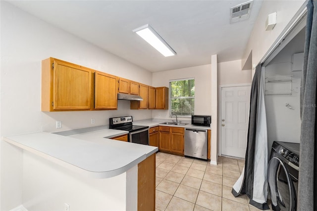 kitchen with under cabinet range hood, a peninsula, light countertops, appliances with stainless steel finishes, and washer / clothes dryer