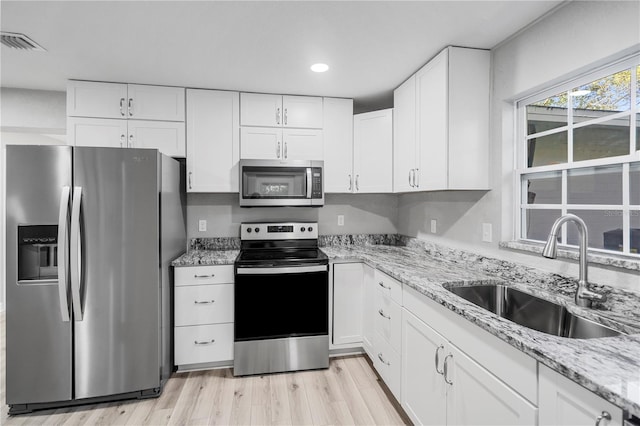 kitchen with stainless steel appliances, sink, light wood-type flooring, light stone countertops, and white cabinetry