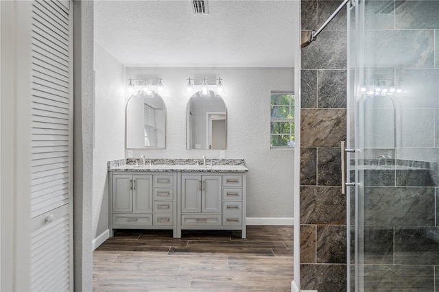 bathroom featuring dual vanity, a shower with door, wood-type flooring, and a textured ceiling