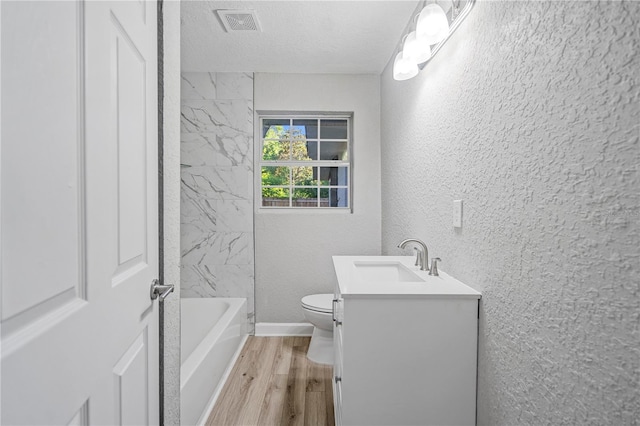 full bathroom featuring vanity, hardwood / wood-style floors, tiled shower / bath combo, toilet, and a textured ceiling