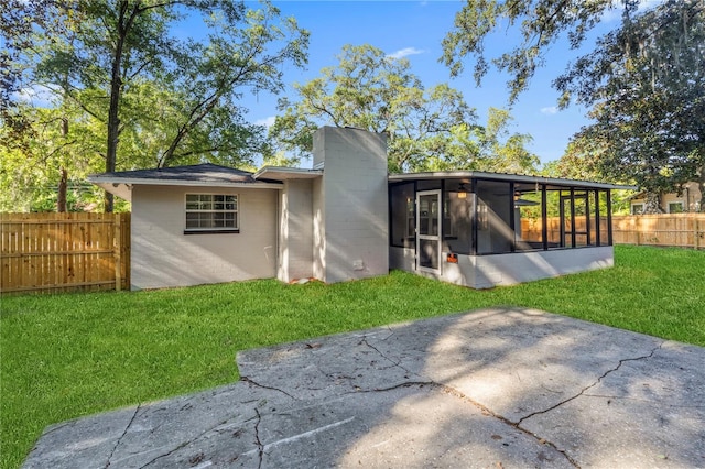 rear view of house with a sunroom, a lawn, and a patio area