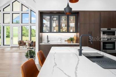 kitchen featuring hardwood / wood-style flooring, dark brown cabinetry, light stone countertops, and double oven