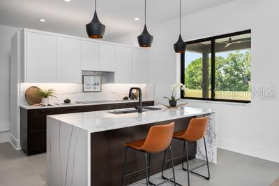 kitchen with decorative light fixtures, sink, white cabinets, light stone countertops, and a center island with sink