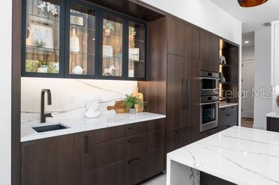 kitchen featuring stainless steel double oven, light stone countertops, sink, and dark brown cabinets