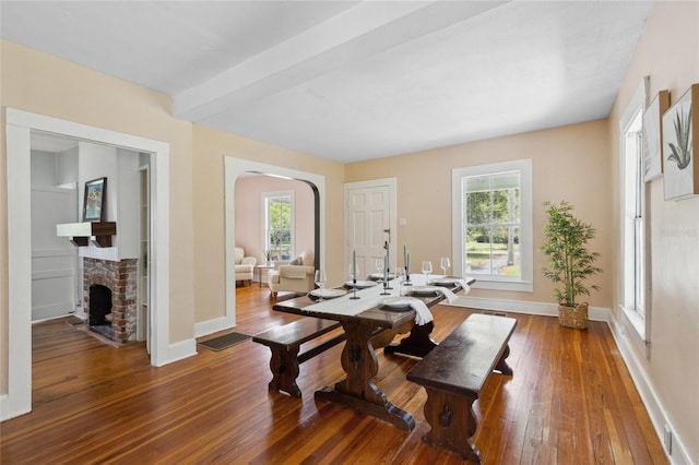 dining space with hardwood / wood-style flooring, plenty of natural light, beam ceiling, and a brick fireplace