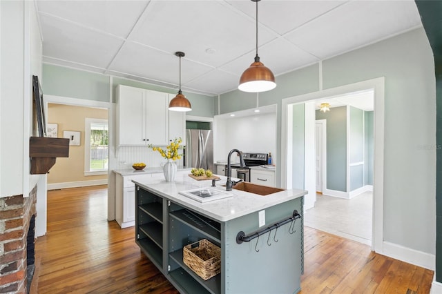 kitchen with stainless steel appliances, white cabinets, hardwood / wood-style floors, hanging light fixtures, and an island with sink