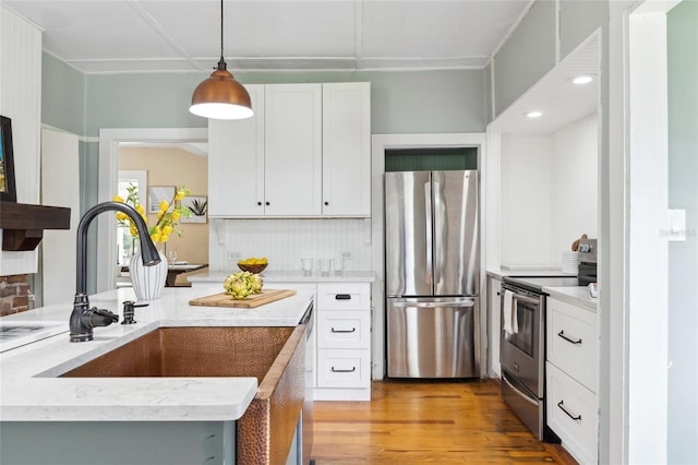 kitchen with appliances with stainless steel finishes, light wood-type flooring, sink, decorative light fixtures, and white cabinetry