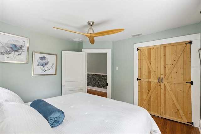 bedroom featuring a barn door, ceiling fan, and dark hardwood / wood-style flooring