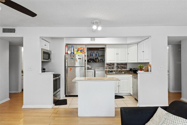 kitchen with appliances with stainless steel finishes, white cabinetry, light wood-type flooring, ceiling fan, and washer and clothes dryer