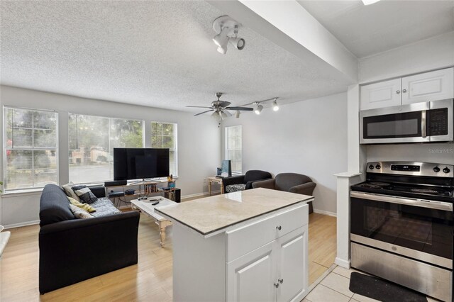 kitchen with light wood-type flooring, ceiling fan, stainless steel appliances, and white cabinets